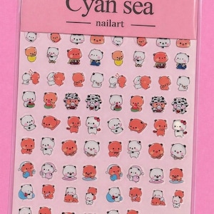 May include: A sheet of nail art stickers featuring various cartoon bear designs in orange, white, and blue. The stickers are packaged in a pink plastic sleeve with the text "Cyan sea nailart" and the product code "CG-227".