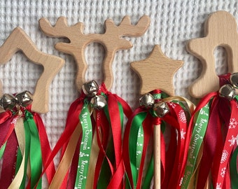 May include: Wooden Christmas-themed wands with star, reindeer, and gingerbread man shapes. Each wand has red, green, and gold ribbons, silver bells, and a wooden handle. The ribbons are printed with "Merry Christmas".