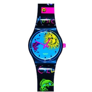 May include: A Swatch watch with a blue face featuring a yellow sun and a pink fish. The black strap has the words "MUSIC" and "CALL" in neon colours, along with a green fish graphic. The watch has a pink accent.