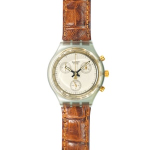 Puede incluir: Un reloj Swatch Swiss con esfera clara, detalles dorados y una correa de cuero marrón. El reloj presenta tres subesferas y una pantalla de fecha. La correa tiene un patrón texturizado similar al de un cocodrilo.