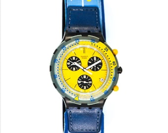 May include: A yellow and blue Swatch chronograph watch with a black face and a blue strap. The watch has a date window at the 4 o'clock position and a tachymeter scale around the outer edge of the face.