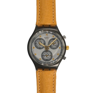 May include: A silver Swatch chronograph watch with a yellow leather band. The watch face has three subdials with a swirling pattern.