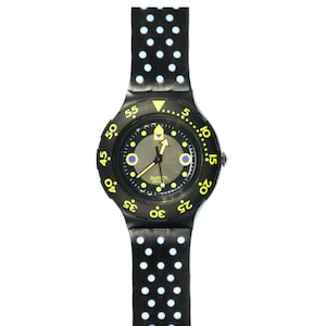 以下が含まれることがあります： 黒と白のドット柄のバンドが付いた、黄色のベゼルと黒色のSwatch腕時計。文字盤は黒で、黄色の目盛りと灰色の背景があります。