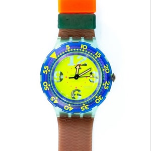 Könnte beinhalten: Eine blaue und grüne Swatch-Uhr mit einem gelben Zifferblatt und einem braunen Kautschukband. Die Uhr hat ein großes, rundes Zifferblatt mit einem schwarzen Stunden- und Minutenzeiger und einem roten Sekundenzeiger. Das Zifferblatt ist von einer blauen Lünette mit weißen Zahlen umgeben.