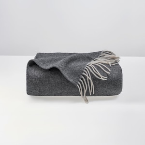 May include: A gray throw blanket with a white fringe. The blanket is folded in half and has a herringbone pattern.