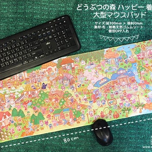 May include: A large mouse mat featuring a colourful illustration of Animal Crossing characters and scenery. The mat measures 30 cm by 80 cm and is made of fabric with a natural rubber base. The text on the mat reads "どうぶつの森ハッピー着陸! 大型マウスパッド".