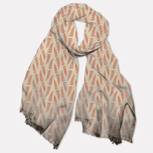 May include: A cream-colored scarf with a repeating pattern of rust-colored fern fronds. The scarf has a fringed edge and is draped to show the pattern. The scarf is made of a soft, lightweight fabric.