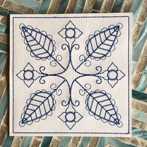 May include: A white square coaster with a blue embroidered design of stylized leaves and flowers.