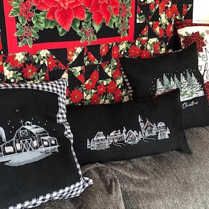 May include: A collection of black decorative pillows with embroidered winter scenes, including a barn, village, and Christmas trees. The pillows have a gingham border and are set against a backdrop of poinsettia fabric.