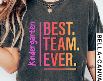 Op de afbeelding: Een donkergrijs T-shirt met de tekst "Kindergarten Best Team Ever." in een regenboogkleurige gradiënt. De tekst staat in een kader met een witte rand.