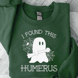 May include: A dark green sweatshirt with a white ghost holding a bone and the text "I found this humerus" printed on the front.