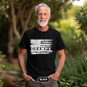 May include: Black t-shirt with a white distressed American flag design. The text "Grampa" is printed in white with the names "Alice, Nicole, Sophia, Sarah, Daniel, Rebecca" printed below. The shirt is being worn by a man with a white beard.