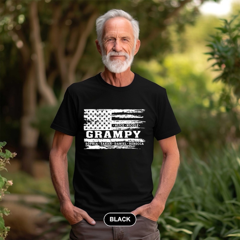 May include: Black t-shirt with a white distressed American flag design. The text "Grampa" is printed in white with the names "Alice, Nicole, Sophia, Sarah, Daniel, Rebecca" printed below. The shirt is being worn by a man with a white beard.
