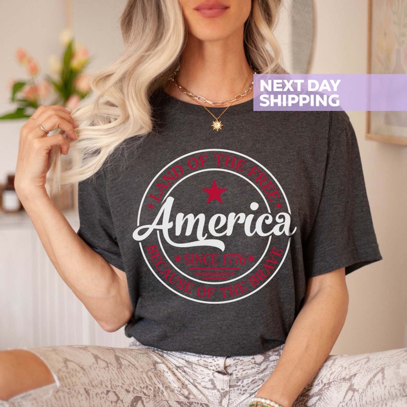 May include: A dark gray t-shirt with a white circle graphic that says "Land of the Free, America, Since 1776, Because of the Brave". The graphic has a red star and red text.