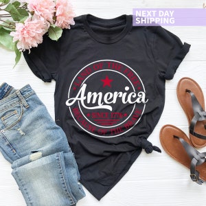 May include: Black t-shirt with a white circle graphic that says "Land of the Free America Since 1776 Because of the Brave".