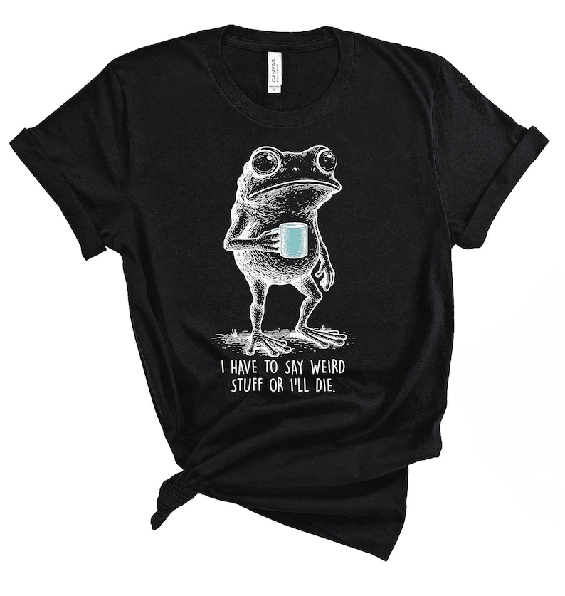May include: Black t-shirt featuring a white illustration of a frog holding a blue mug. The frog has a contemplative expression. The text "I HAVE TO SAY WEIRD STUFF OR I'LL DIE" is below the frog. The shirt is made of a soft material.