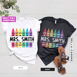May include: Two t-shirts, one white and one black, with a design of rainbow crayons and the text "MRS. SMITH".