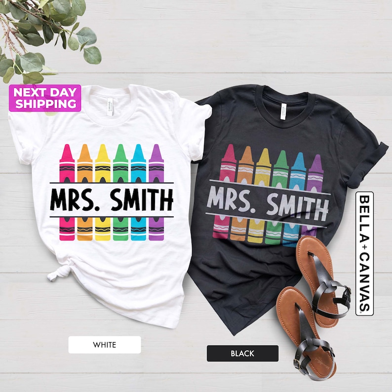 May include: Two t-shirts, one white and one black, with a design of rainbow crayons and the text "MRS. SMITH".