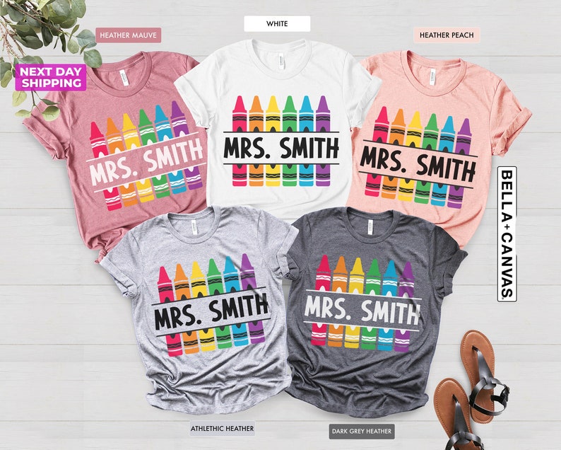 May include: Five different colored t-shirts with the text "MRS. SMITH" and a rainbow of crayons. The t-shirts are heather mauve, white, heather peach, athletic heather, and dark grey heather.
