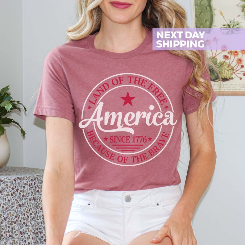 May include: A maroon t-shirt with a white circle graphic that says "Land of the Free America Because of the Brave" with a red star and the text "Since 1776" inside the circle.