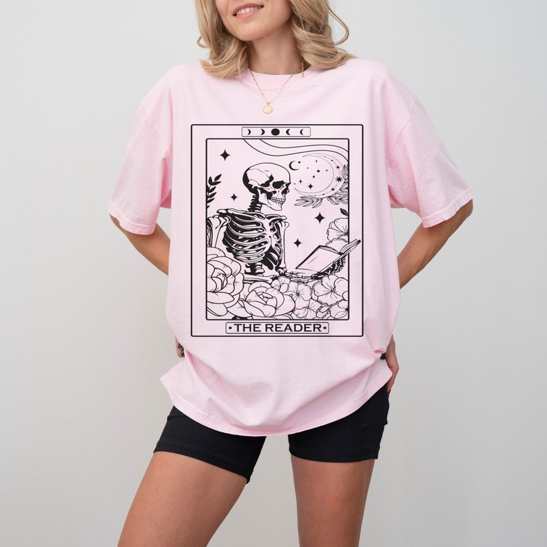May include: Pink oversized t-shirt with a black and white tarot card design featuring a skeleton reading a book. The card reads "THE READER".