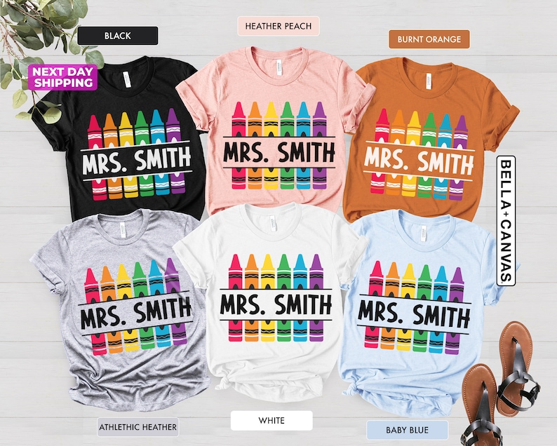 May include: A set of ten t-shirts in various colors featuring a rainbow of crayons with the text "MRS. SMITH" printed on each shirt.