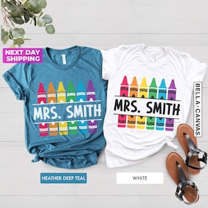 May include: Two t-shirts with a design of colorful crayons and the text "MRS. SMITH". The t-shirts are in teal and white.