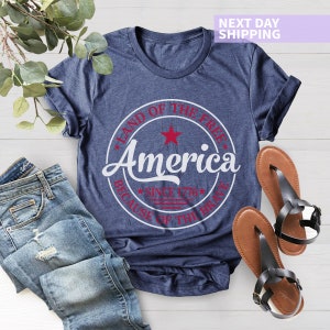 May include: A navy blue t-shirt with a white circle graphic that says "Land of the Free, America, Since 1776, Because of the Brave". The graphic has a red star and red stripes.