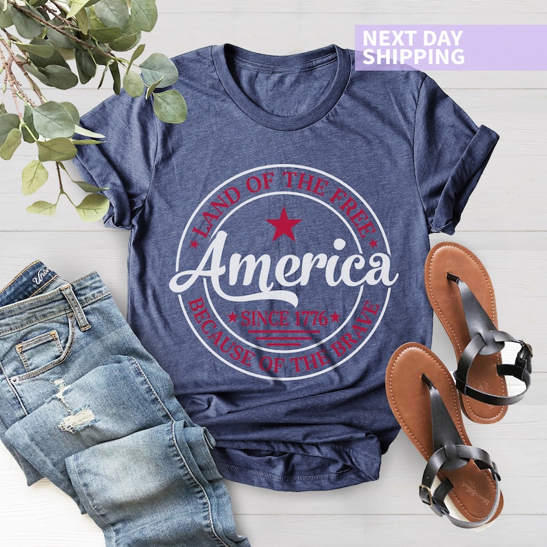 May include: A navy blue t-shirt with a white circle graphic that says "Land of the Free, America, Since 1776, Because of the Brave". The graphic has a red star and red stripes.
