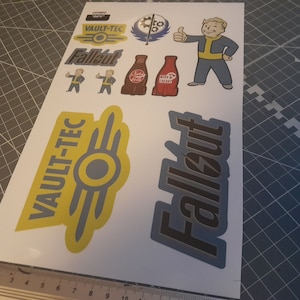 May include: A sheet of Fallout stickers. Designs include the Vault-Tec logo, Fallout logo, Vault Boy character, and Nuka-Cola bottles. The stickers are in yellow, blue, red, and brown.