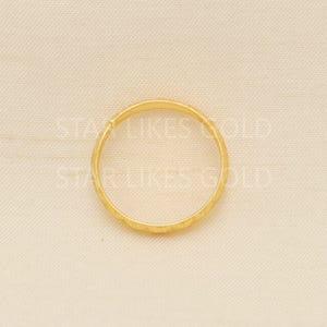 May include: A gold ring with a textured surface. The ring is circular and appears to be made of a shiny, yellow metal. The ring is set against a neutral background.