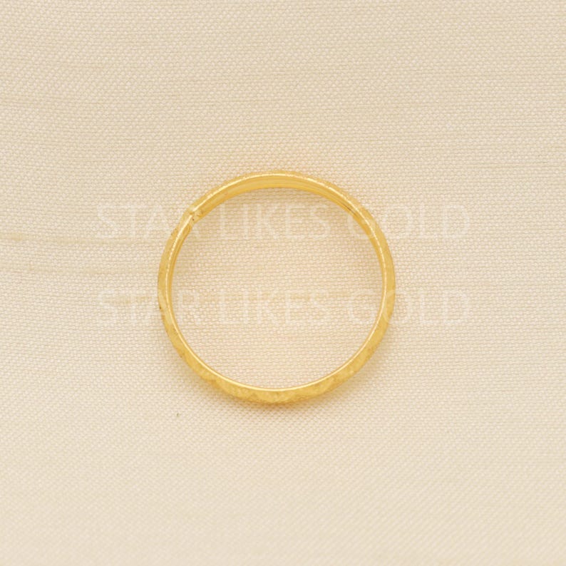 May include: A gold ring with a textured surface. The ring is circular and appears to be made of a shiny, yellow metal. The ring is set against a neutral background.