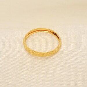 May include: A gold ring with a geometric pattern. The ring is a thin band with a repeating diamond-like design around the exterior. The ring is set against a neutral background.