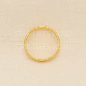 May include: A gold ring with a textured surface. The ring is circular and appears to be made of a shiny, yellow metal. The ring is set against a neutral background.
