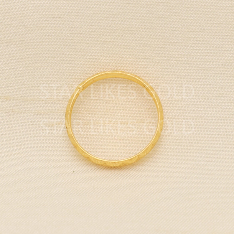 May include: A gold ring with a textured surface. The ring is circular and appears to be made of a shiny, yellow metal. The ring is set against a neutral background.