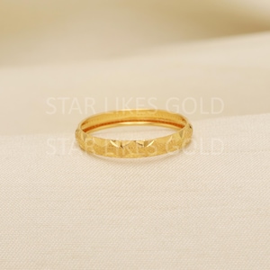 May include: A gold ring with a geometric design. The ring is a bright, shiny gold colour and features diamond-shaped indentations around the band. The text "STAR LIKES GOLD" is visible in the background.