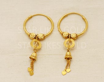 May include: A pair of gold hoop earrings with a dangling charm. The charm is a small bell with a chain and two heart-shaped pendants.