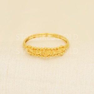 Op de afbeelding: Een gouden ring met een centrale band met een herhalend druppelpatroon, omrand door twee rijen kleine, bolvormige kralen. De tekst STAR LIKES GOLD is zichtbaar op de achtergrond. De ring heeft een gepolijste afwerking en een ronde vorm.