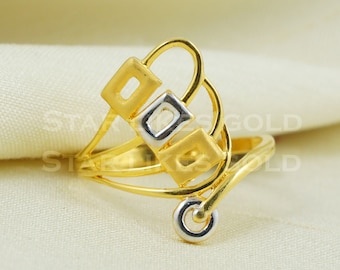May include: A gold-colored ring with a unique design. The ring features three square shapes, one silver-colored and two gold-colored, connected by curved lines. A small silver circle is at the base of the design.