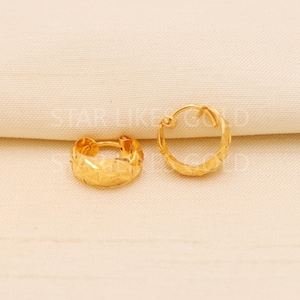 May include: A pair of small gold hoop earrings featuring a textured, faceted surface that reflects light. The earrings have a hinged closure mechanism and a polished finish, showcasing a repeating geometric pattern across the circular bands.