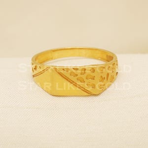 Könnte beinhalten: Ein goldfarbener Ring mit rechteckiger Oberfläche und Muster. Der Ring hat diagonale Linien und eine strukturierte Oberfläche, die einen klassischen Stil zeigt. Der Ring ist ein Schmuckstück.