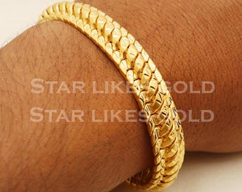 May include: A gold-tone snake chain bracelet with a textured design. The bracelet is worn on a person's wrist.