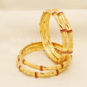 May include: Gold bangles with detailed floral and geometric designs. The bangles feature red and gold accents. The image shows several bangles stacked together. The text "STAR LIKES GOLD" is visible in the background.
