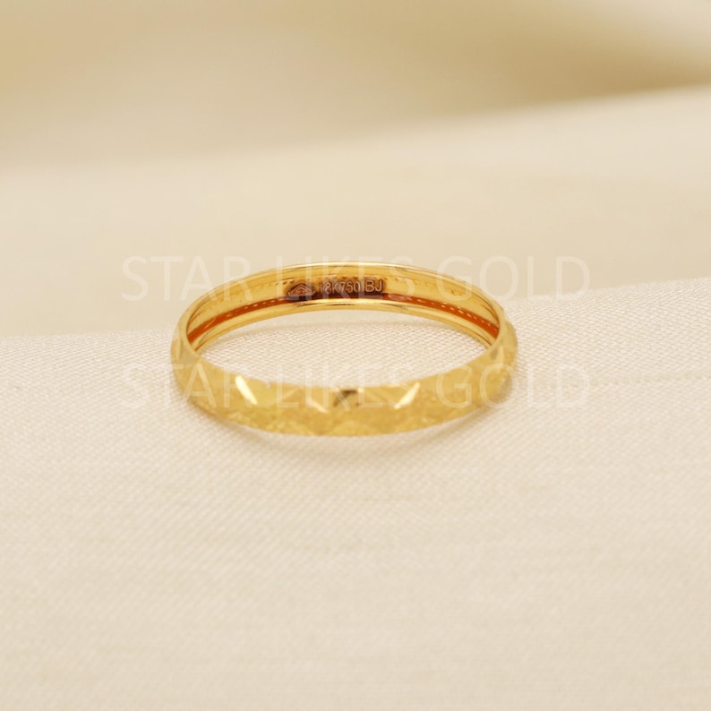 May include: A gold ring with a textured, geometric pattern. The ring is a band style, with a repeating diamond-like design around the exterior. The ring is set against a neutral background.