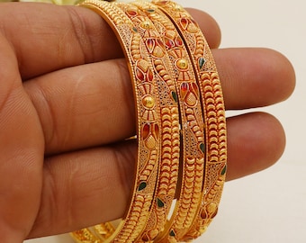 Könnte beinhalten: Ein Set aus drei goldfarbenen Armreifen mit komplexen Filigranmustern, erhabenen Texturen und kleinen Akzenten aus roter und grüner Emaille. Die Armreifen haben eine polierte metallische Oberfläche mit detaillierten Gravuren.