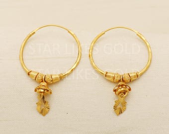 May include: A pair of gold hoop earrings with a small, decorative charm hanging from each hoop. The charms are shaped like a flower with a swirl design.