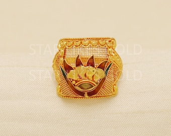 May include: A gold-colored ring with an ornate floral design. The ring features a central floral motif with detailed petals and leaves, and a decorative band. The ring has a textured surface and is set against a neutral background.