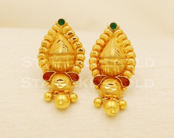 Può includere: Un paio di orecchini color oro con un design dettagliato. Ogni orecchino presenta un elemento centrale ornato con una gemma verde. Gli orecchini hanno un aspetto stratificato e strutturato con un fondo sferico pendente.