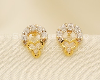 May include: A pair of gold earrings with a circular design featuring small white stones and a dangling clover-shaped charm.