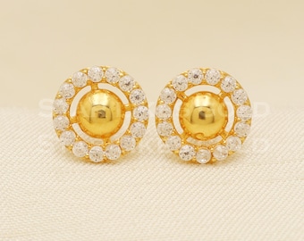 May include: A pair of gold stud earrings with a round, clear crystal halo around a gold ball in the centre.